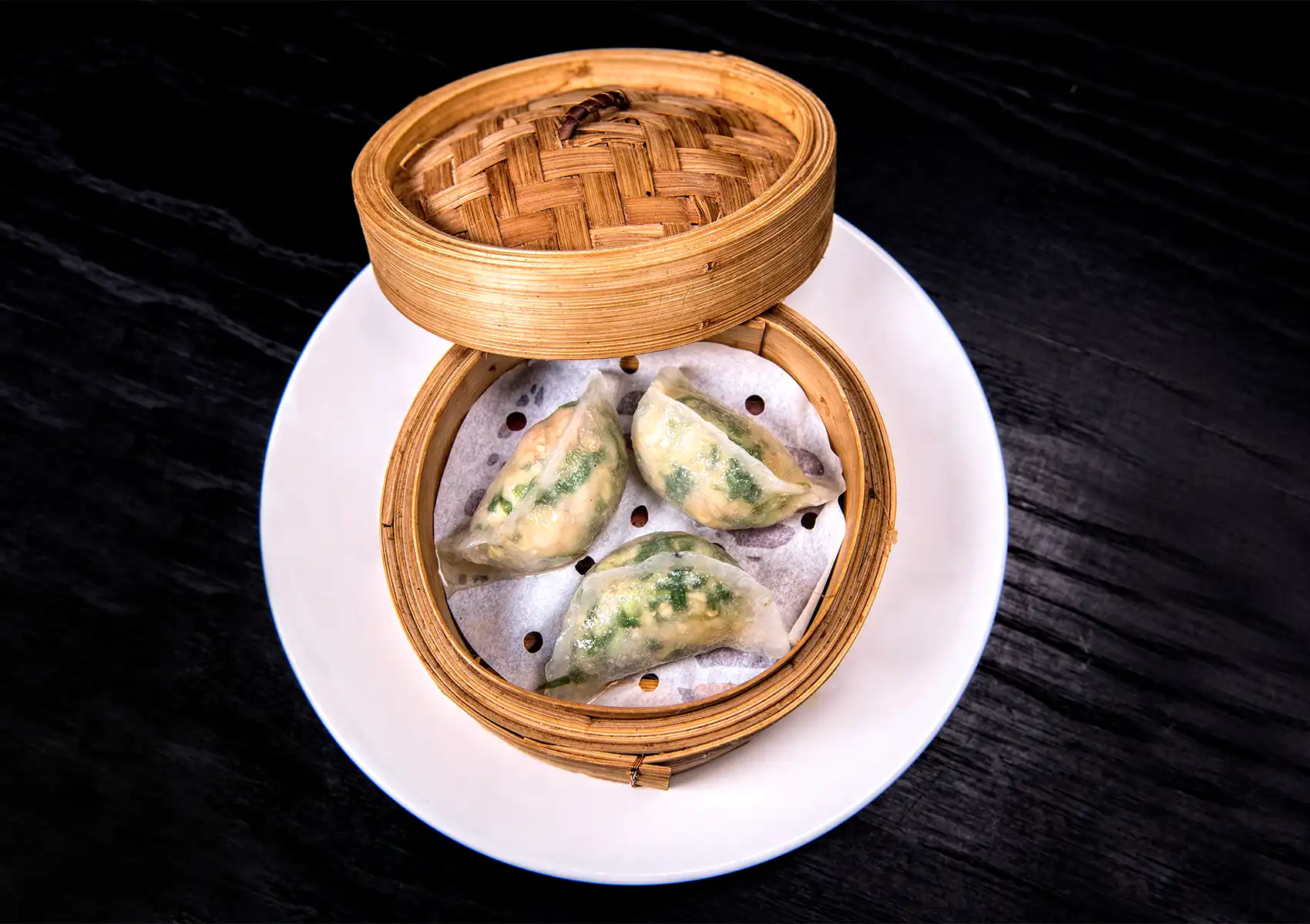 Steamed dumplings in bamboo steamer with translucent wrappers and fresh vegetable filling on wooden table.