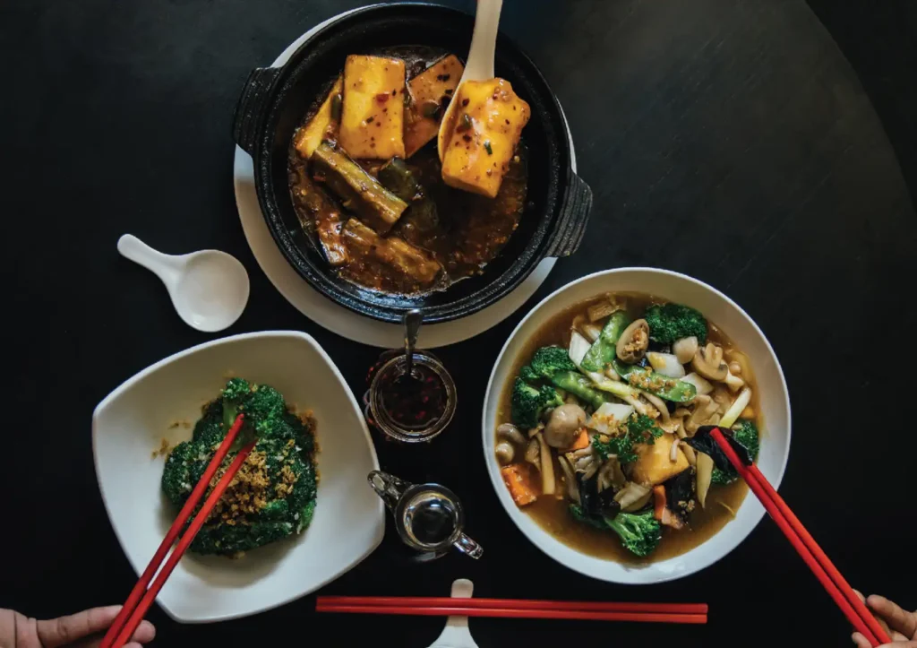 Vegetarian Chinese food with tofu clay pot, stir‑fried greens, and mixed vegetables served with chopsticks.