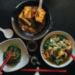 Vegetarian Chinese food with tofu clay pot, stir‑fried greens, and mixed vegetables served with chopsticks.