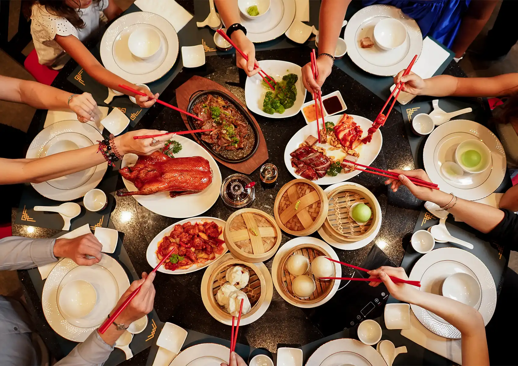 Chinese family restaurant in Bali with group sharing roast duck, steamed buns, and traditional dishes at round table.