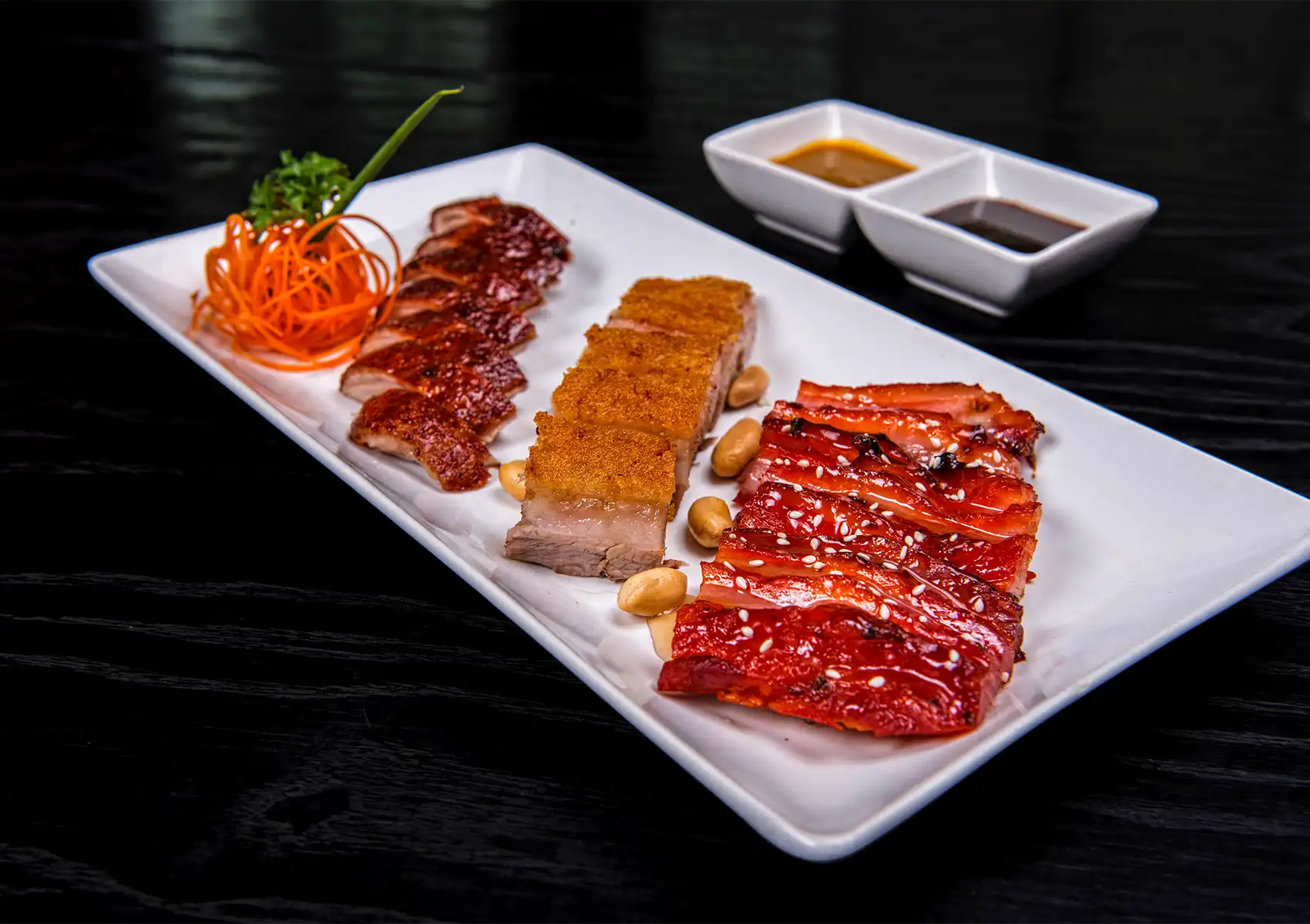 Chinese roasted meat platter with duck, crispy pork belly, and char siu slices elegantly served with sauces.