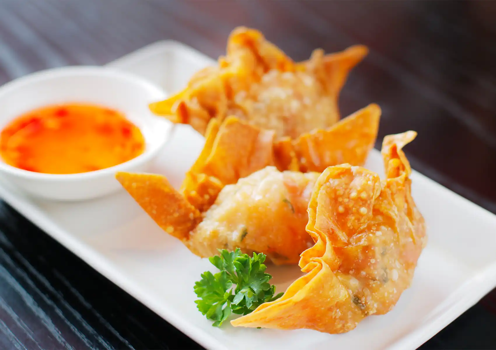 Crispy fried wontons with sweet chili dipping sauce served on a white plate, garnished with parsley.