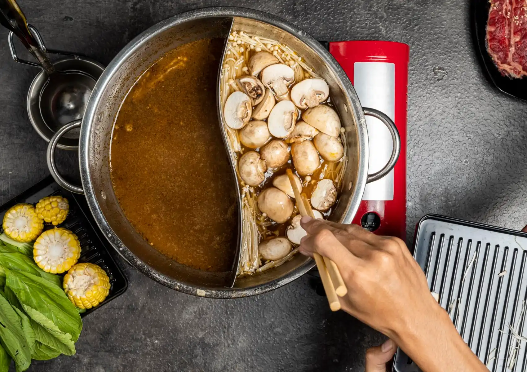 Chinese hot pot with dual broths, mushrooms, and fresh ingredients on dining table.
