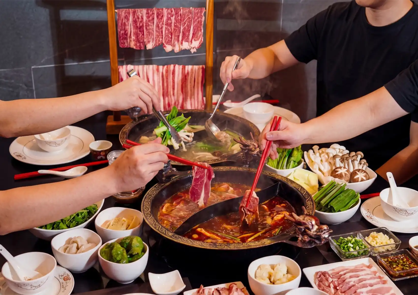 Group enjoying hot pot in Bali with dual broths, sliced meats, mushrooms, tofu, and vegetables for communal dining.