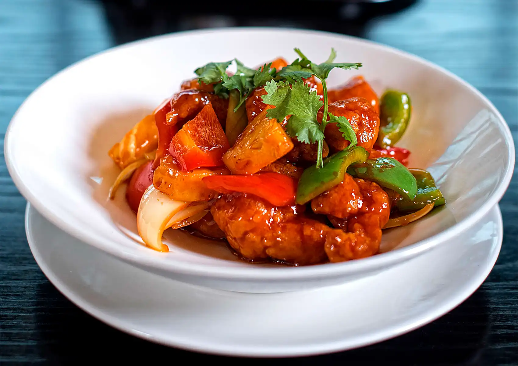 Sweet and sour chicken with pineapple, bell peppers, and onions in glossy sauce, garnished with fresh cilantro.