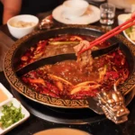 cantonese style hot pot with ornate dragon pot, spicy chili broth, mild herbal soup, and assorted condiments for communal dining.