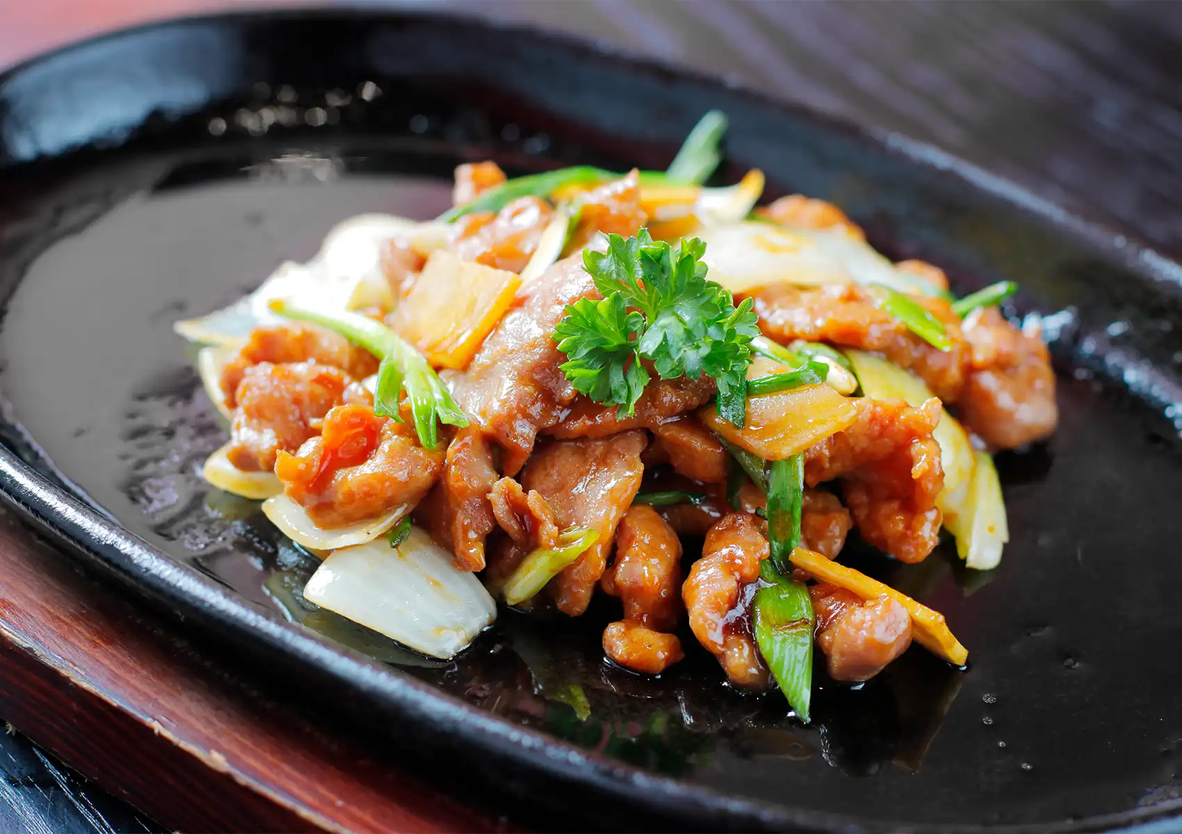 A sizzling plate of ginger and spring onion chicken at a Cantonese restaurant in Bali, with glazed chicken pieces, onions, and fresh herbs, garnished with parsley.