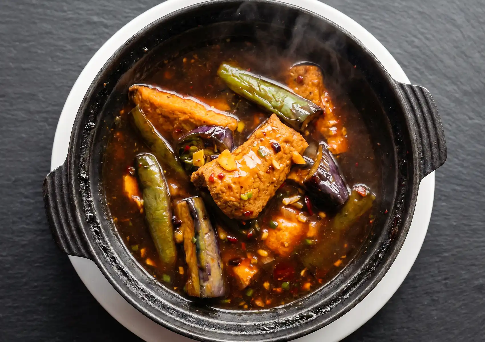 A steaming claypot of vegetarian eggplant and tofu in savory brown sauce with green chilies at a Cantonese restaurant in Bali.