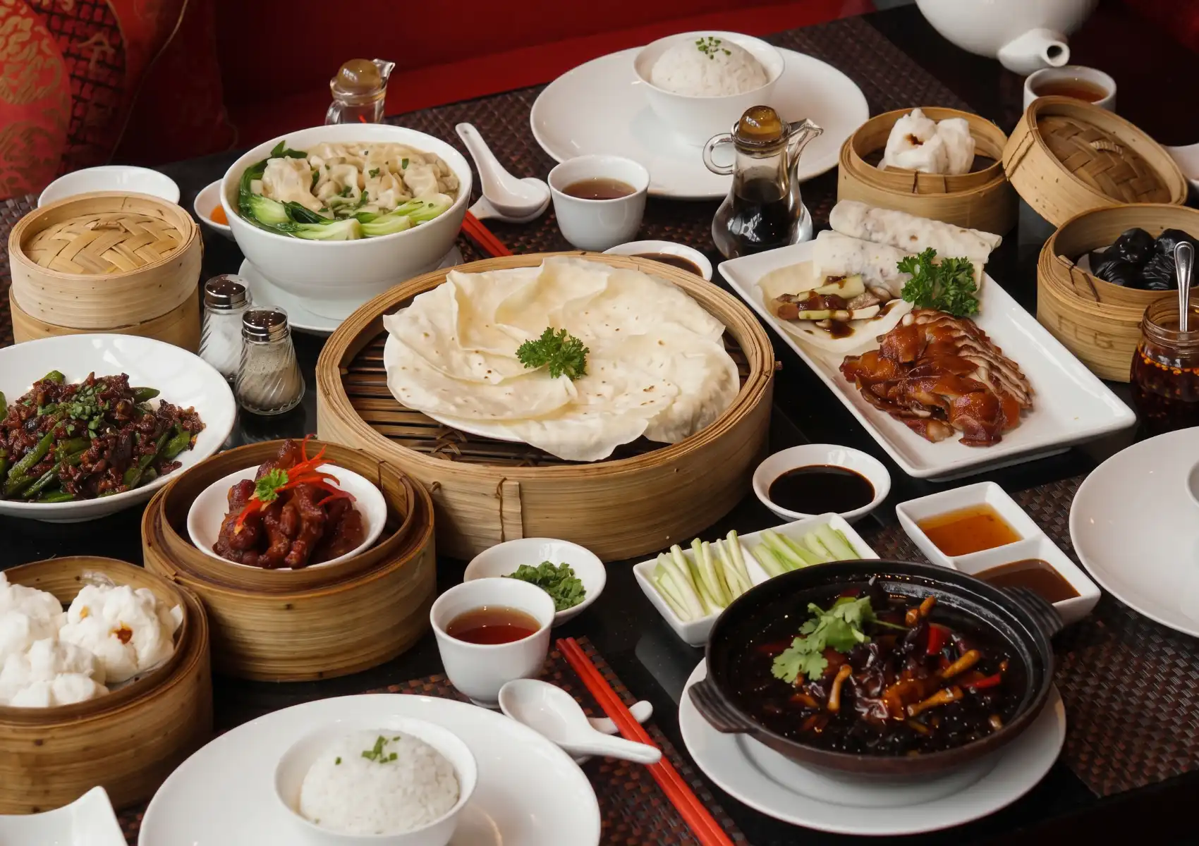 A full table spread at a Cantonese restaurant in Bali, featuring sliced Peking duck, bamboo steamers of dim sum and pancakes, dumpling soup, stir-fried green beans, steamed rice, claypot dishes, and dipping sauces.