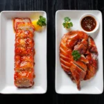 Overhead view of two white plates on a dark wooden table, one featuring sweet glazed char siew pork and the other savory sliced roast duck with dipping sauce, offering a classic Cantonese BBQ Ubud dining experience.