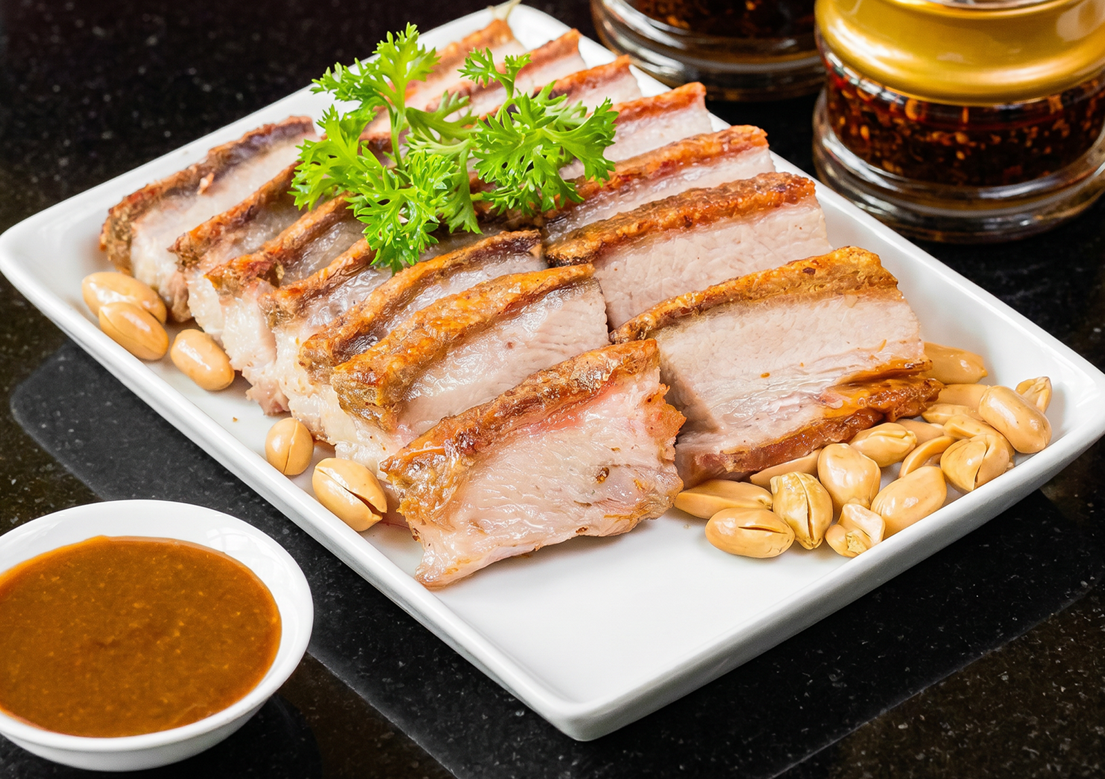 A close-up of thick, juicy slices of crispy roasted pork belly garnished with fresh parsley and scattered peanuts, served alongside a small bowl of dipping sauce at a Cantonese restaurant in Bali.